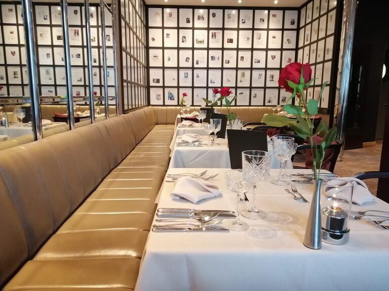 VIP Ecke des Restaurants mit Bildern von prominenten Gästen an der Wand, eingedeckte Tafel mit Tischdecke und Blumen