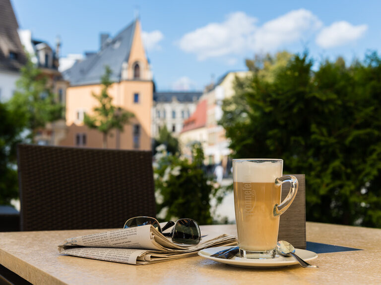 Auf einem Tisch steht eine Tasse Kaffee neben einer Zeitung